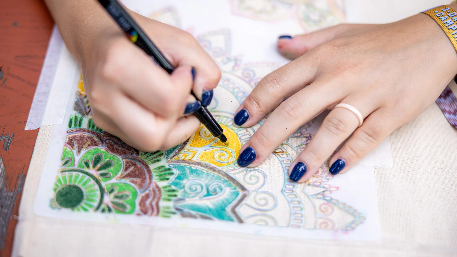 Detailaufnahme einer Hand, die mit einem Textilstift ein buntes Mandala-Muster auf eine Stofftasche malt – Teil des Taschen-Workshops beim San Hejmo Festival.