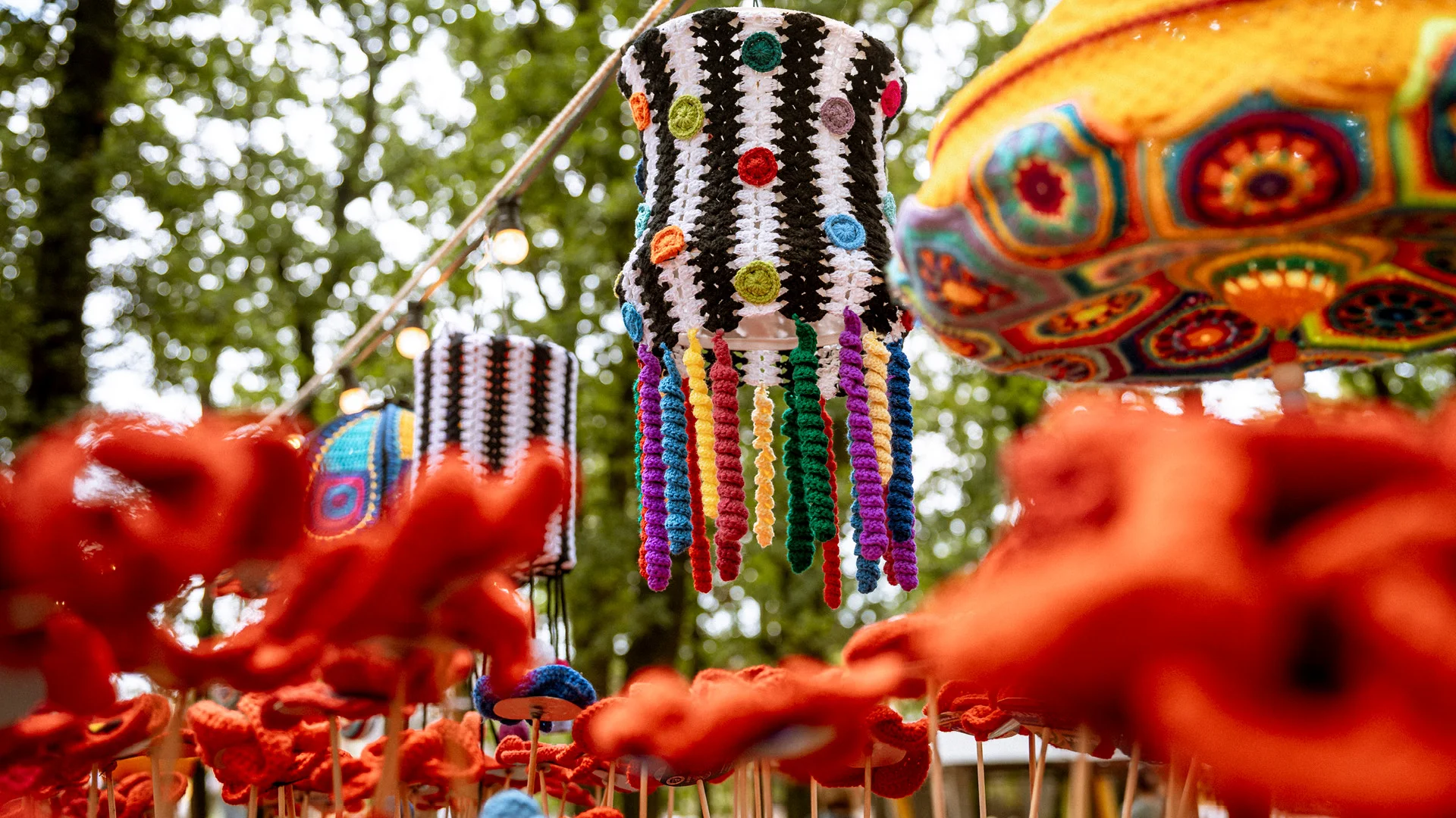 Gehäkelte Lampenschirme und leuchtend rote Häkelblumen als verspielte Kunstinstallation im Wald des San Hejmo Festivals.